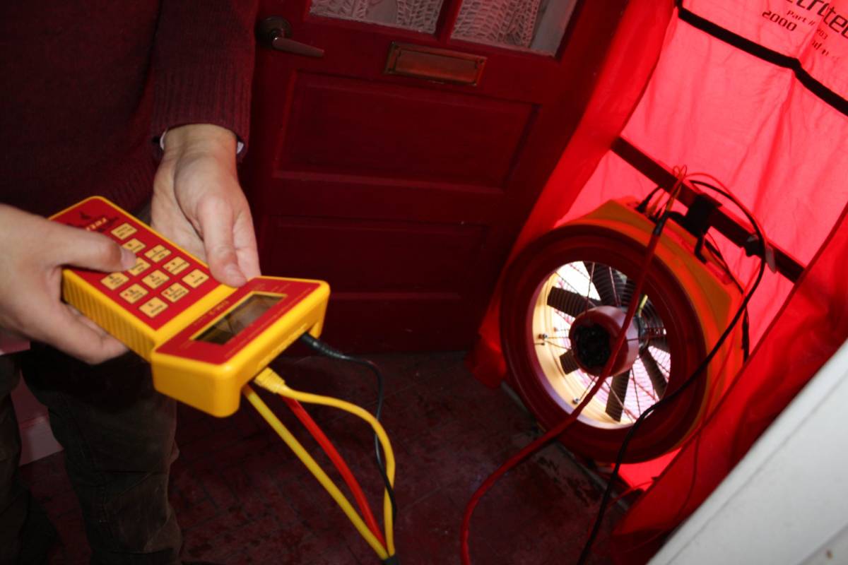 Ventilator Blower Door uređaja postavljen u okvir ulaznih vrata, uz manometar u ruci